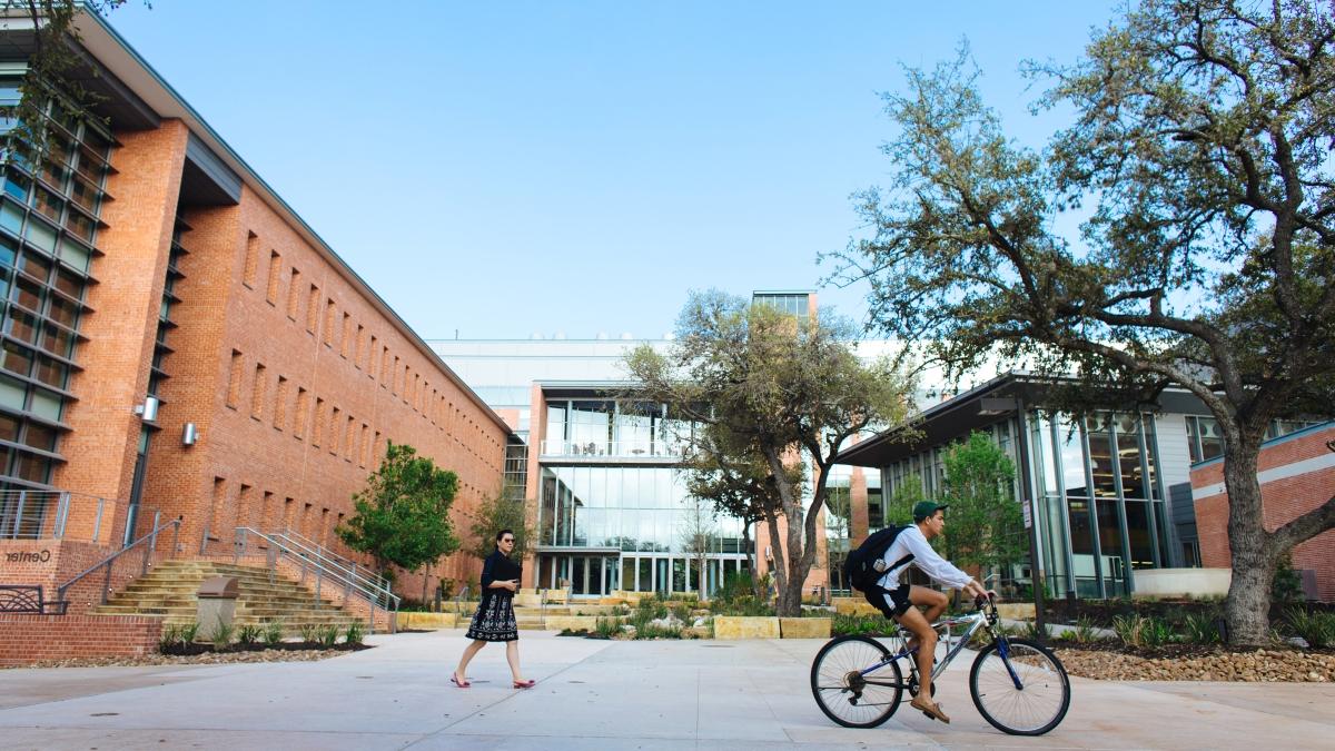 a student on a bicycle rides by the entrance to CSI